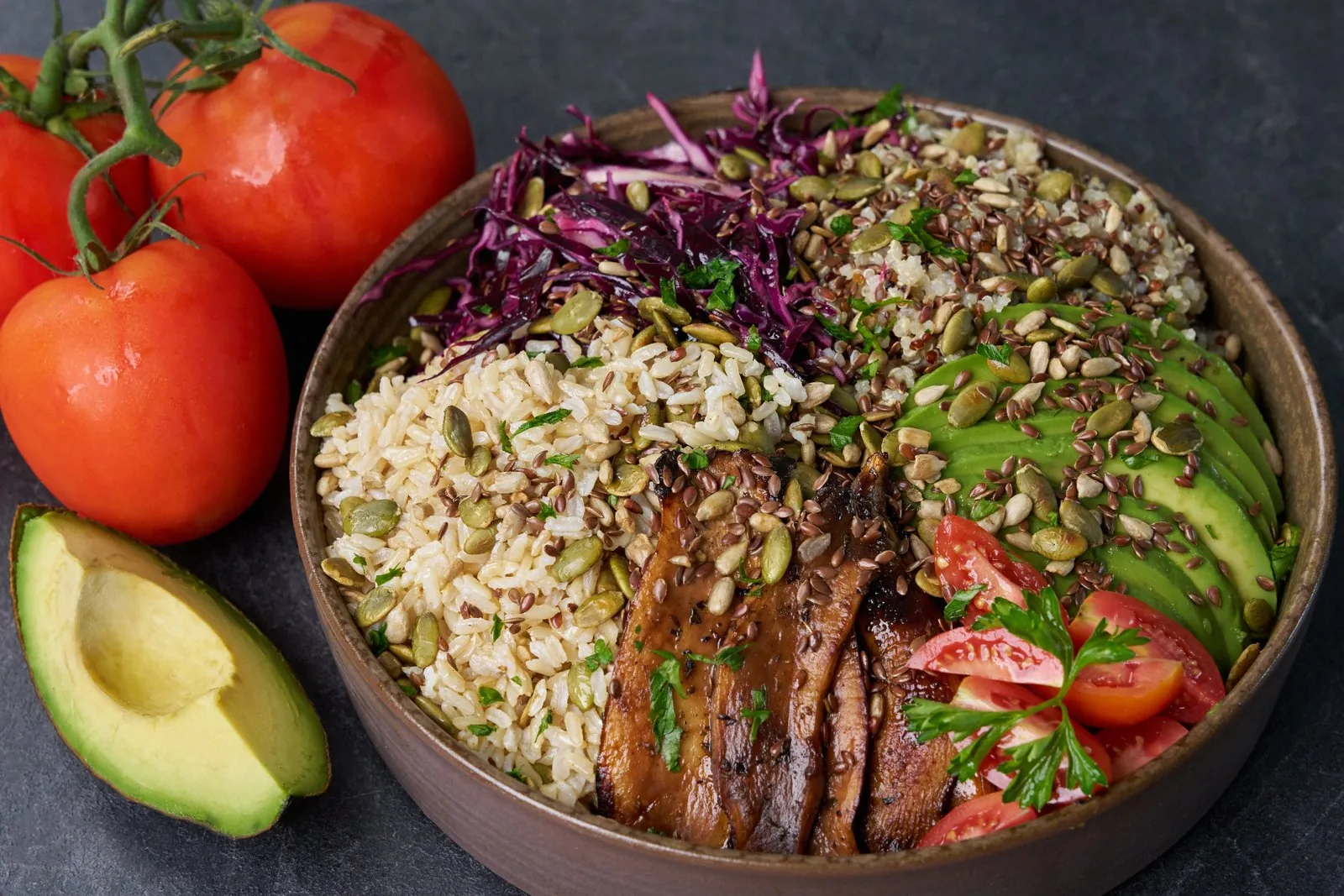 Professional food bowl with grilled meat, rice, purple cabbage, avocado, tomatoes, and fresh herbs
